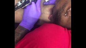 Mischievous tattoo artist multi-tasking blowing client's nipples